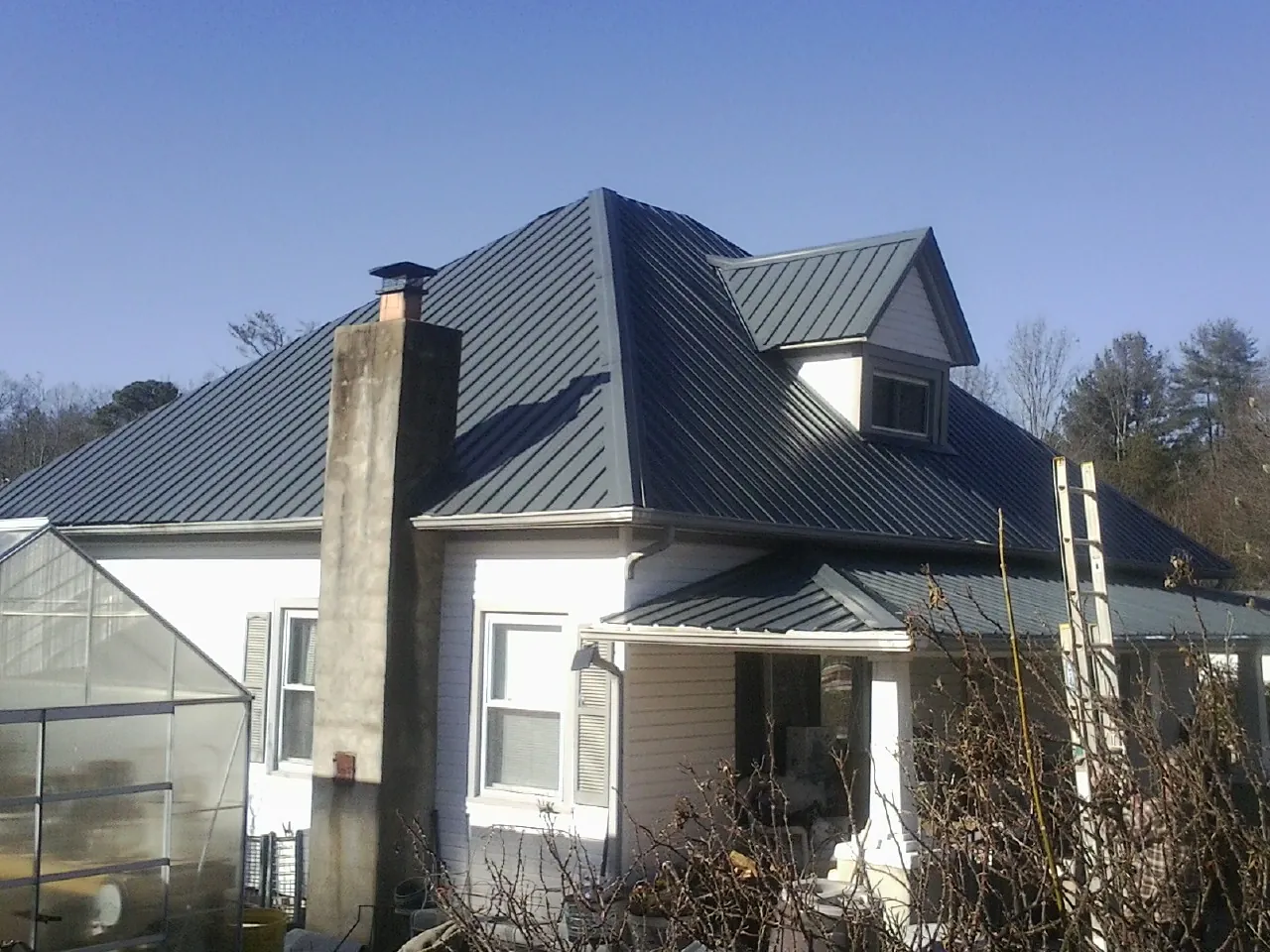 Dark blue standing seam metal roof on a white farmhouse with dormer — Slate & Tile Roof Repair by Roofing Brothers in Moore