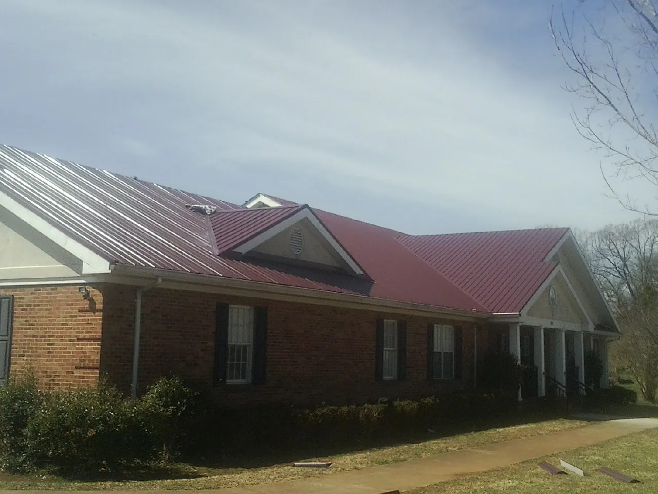 Red metal roof with gabled entries on a long brick building, from a Hail Damage Roof Repair job in Moore