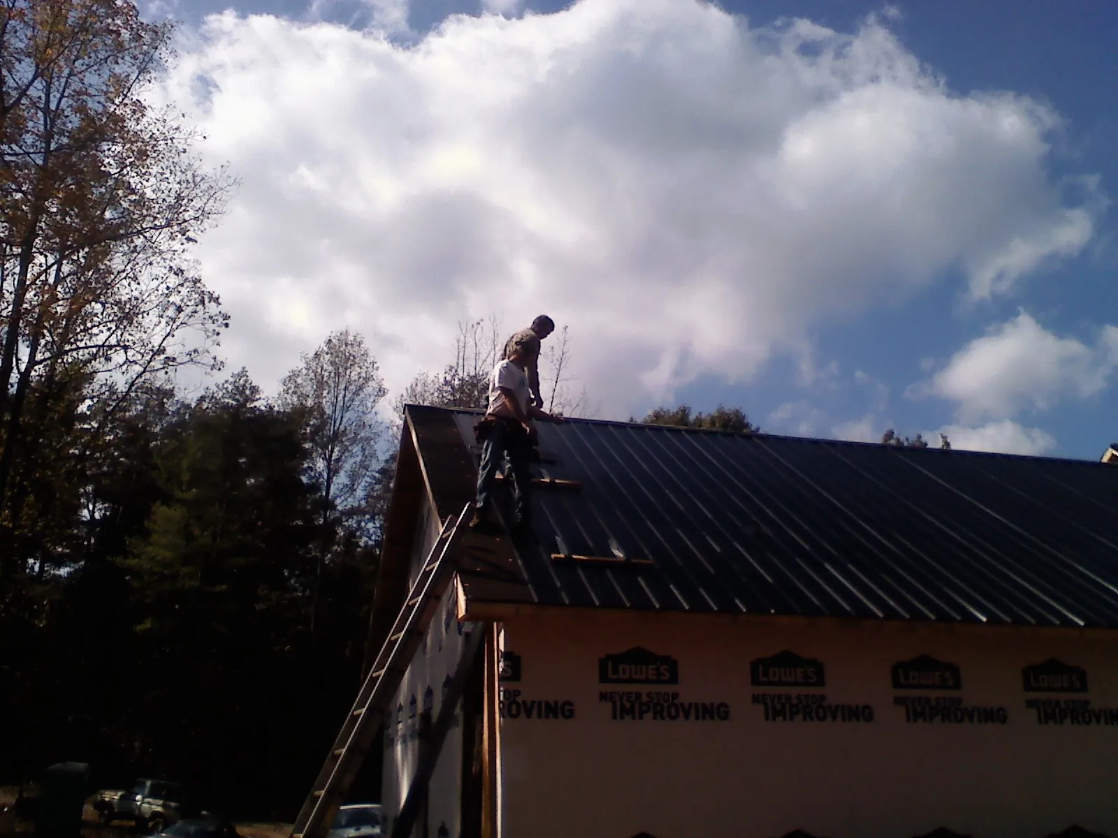 Roofer fastening dark metal panels high against a cloudy sky, from a Roof Inspection job in Moore